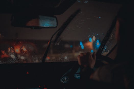 Moody night drive in Manchester with neon lights reflecting on wet windshield.