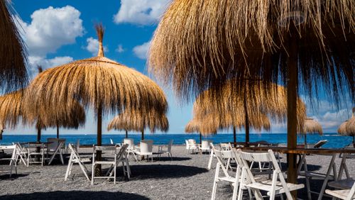 Free Serene beach scene with thatched umbrellas and chairs under a sunny sky in Adeje, Spain. Stock Photo