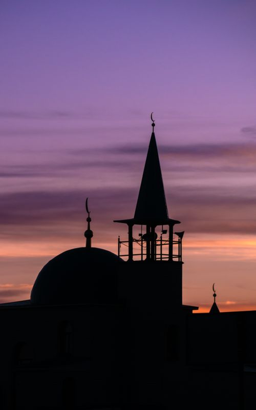 Free A dramatic silhouette of a mosque dome and minaret against a vibrant sunset sky. Stock Photo