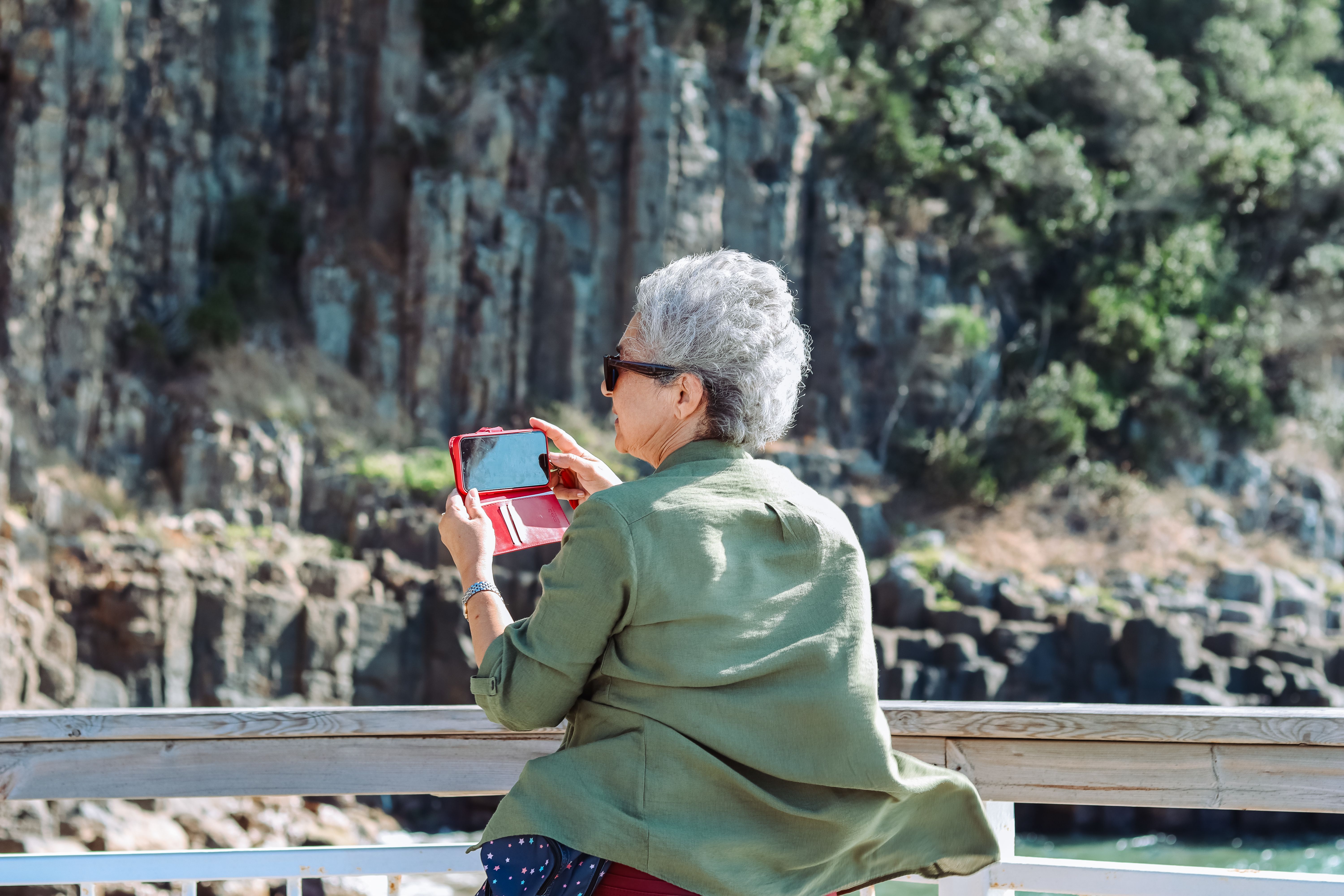Elderly woman takes photos of a canyon with her smartphone on a sunny day.