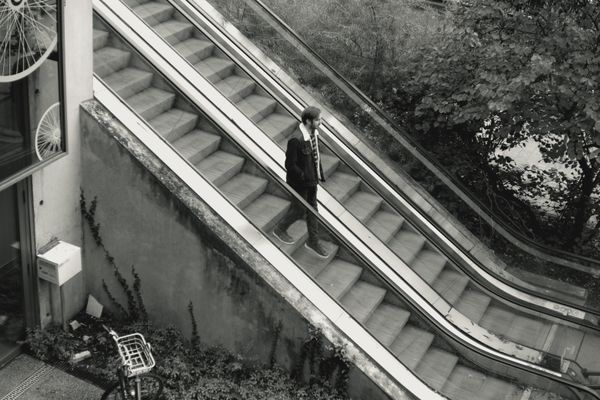 Homme en costume sur un escalator extérieur en noir et blanc