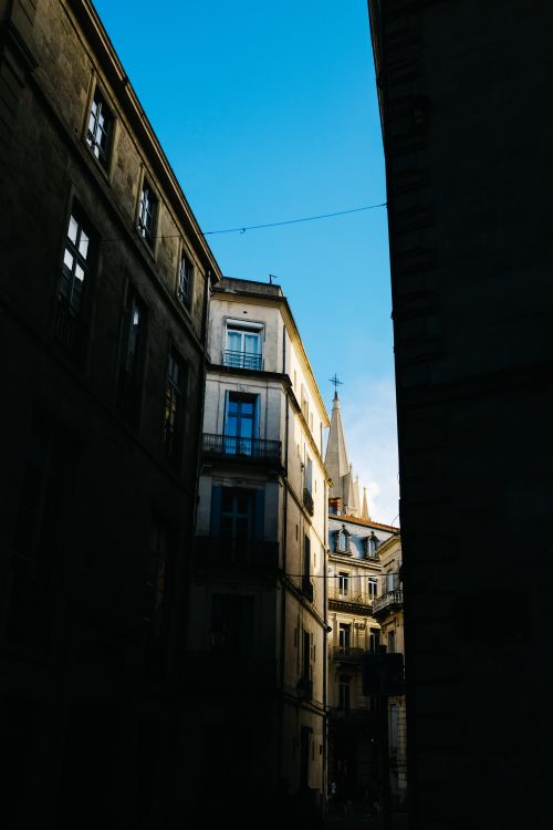 Free Sunlit historic buildings with church spire peeking through urban alleyway. Stock Photo