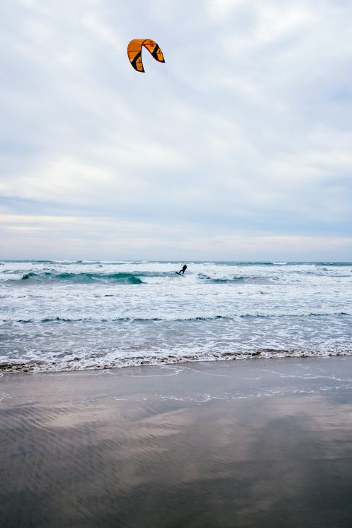 Free Kitesurfer rides the waves on a calm beach day, showcasing adventure and thrill. Stock Photo