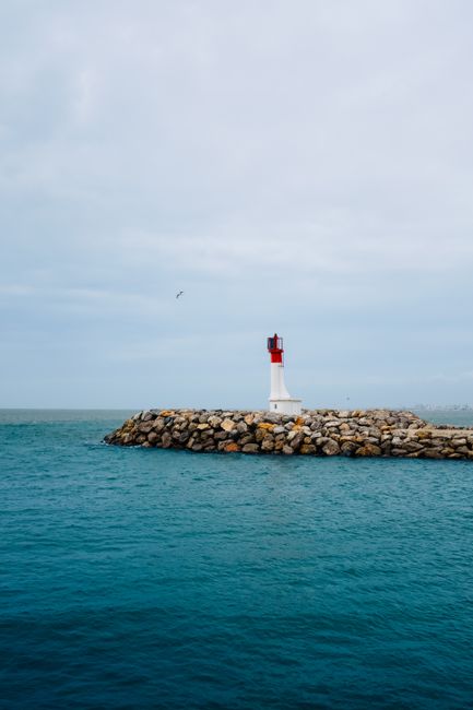 A solitary lighthouse stands on a rock formation surrounded by the tranquil sea under a cloudy sky.