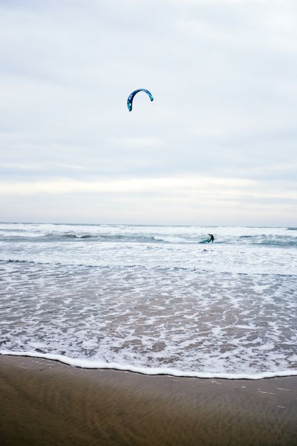 Kitesurfer riding waves under a clear sky, enjoying an adventure-filled day at the beach.