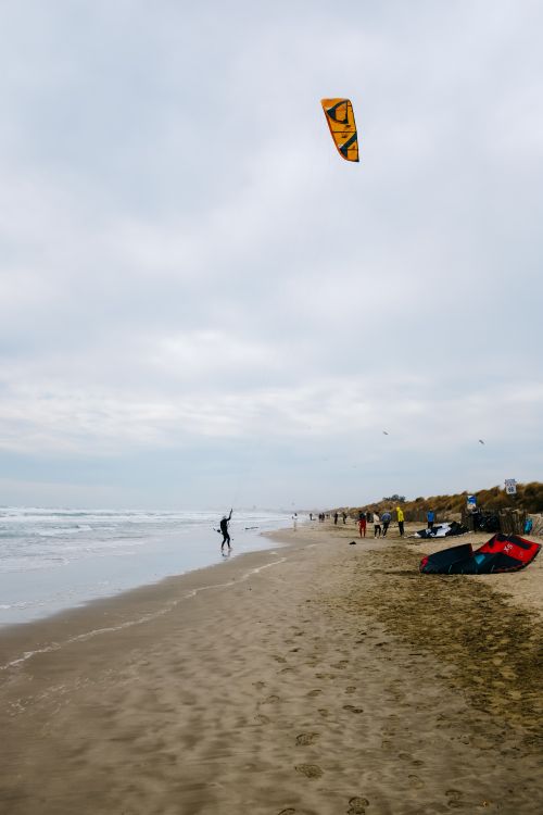 Free A vibrant scene of kitesurfing on a sandy beach with waves and people enjoying leisure activities. Stock Photo