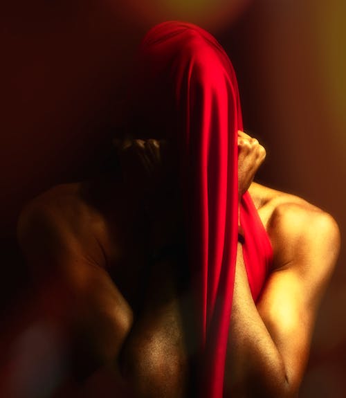 Photo of a Shirtless Man with His Head Covered by Red Fabric 