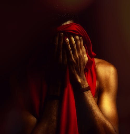 A Shirtless Man Hiding His Face in Red Fabric 