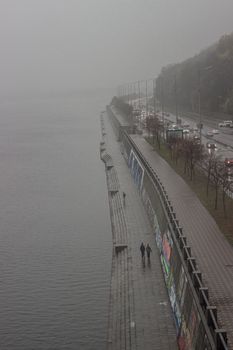Aerial view of a foggy riverside walkway with traffic and pedestrians.