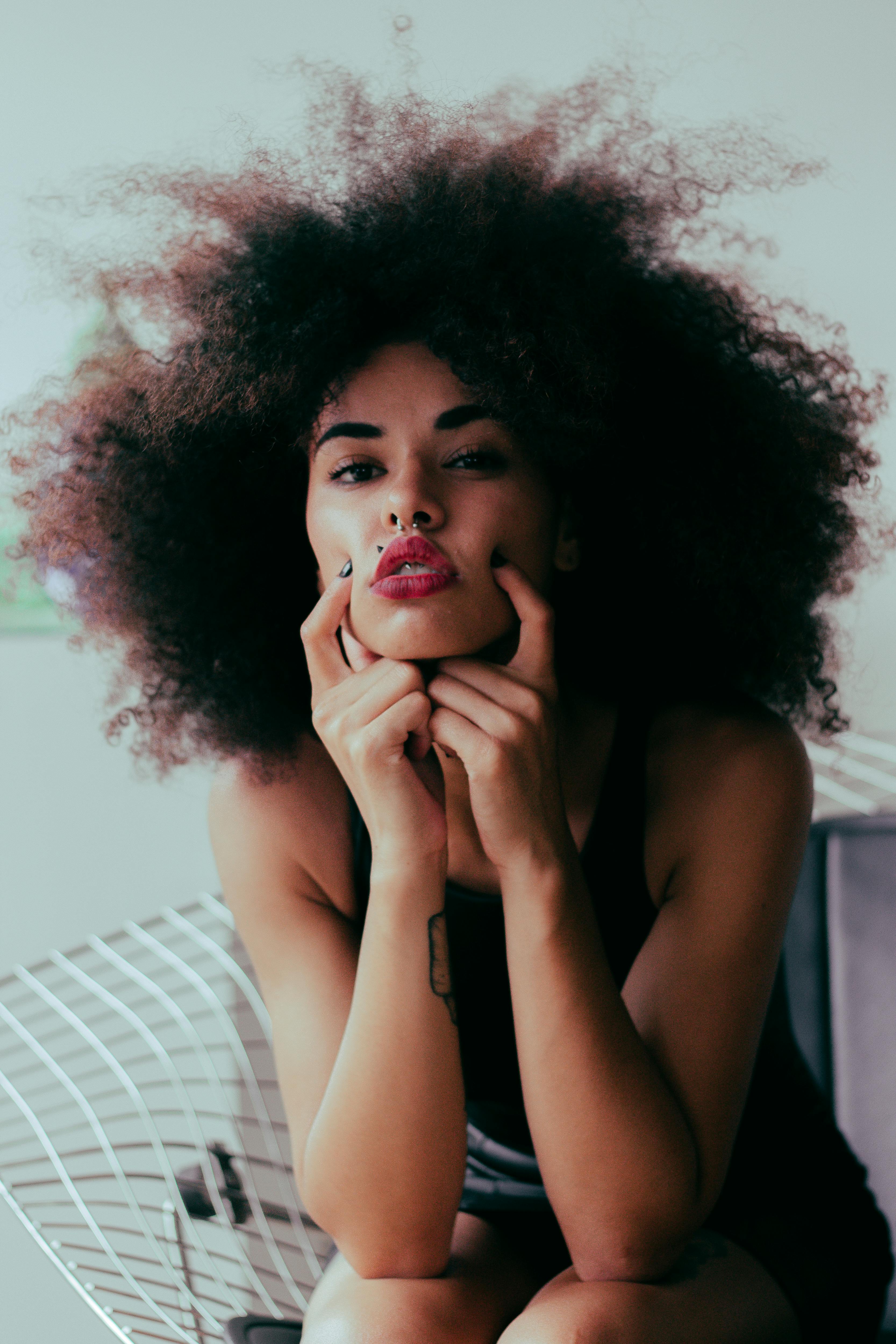 这幅肖像画描绘了一位卷发、纹身、红唇、姿势时尚的迷人女子