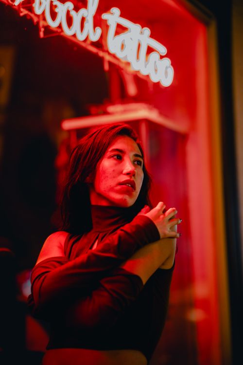 Free A woman in a stylish outfit stands under red neon lights in an urban setting at night. Stock Photo