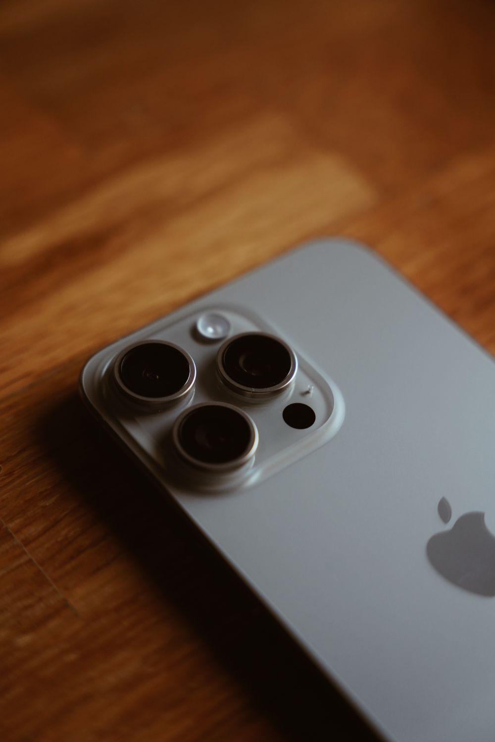 Should You Wait for the iPhone 18 Pro Max? Here's What Apple Fans Need to Know 6 A detailed close-up of an iPhone lying on a wooden table showcasing its triple camera system