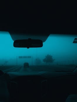 View from inside a car driving on a foggy road with low visibility, creating a mysterious atmosphere.