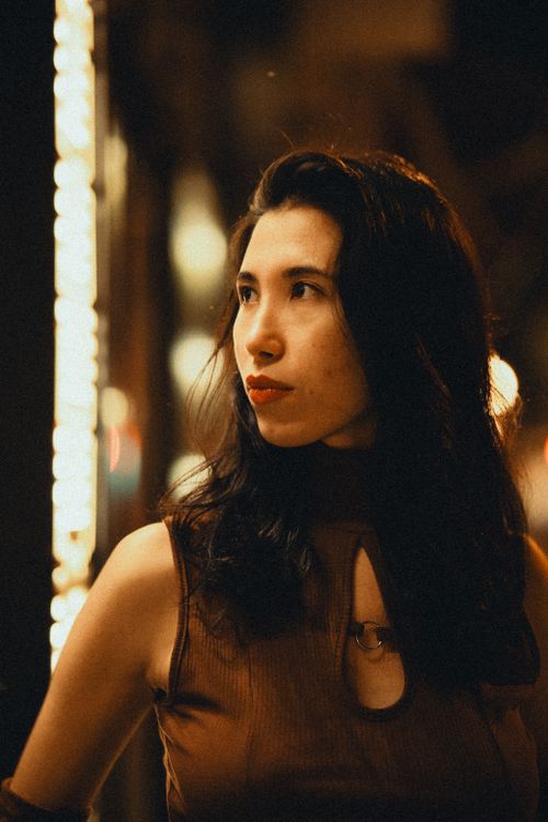 Free Captivating portrait of a woman with long dark hair, bathed in warm night lights. Stock Photo