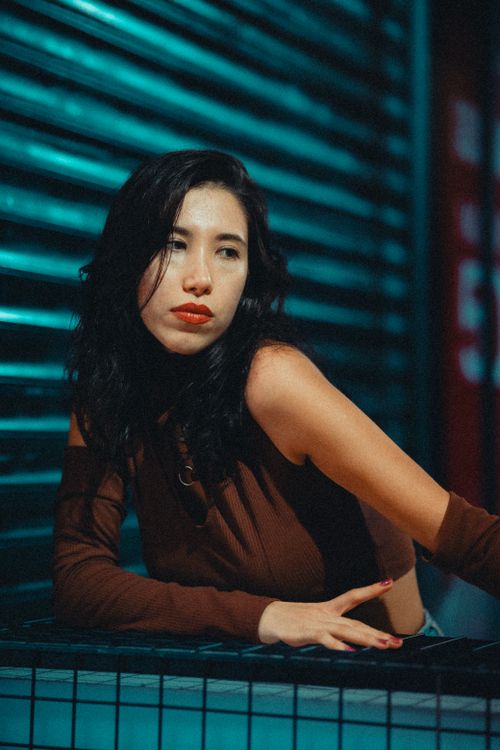 Free Portrait of a woman with black hair leaning against an urban wall at night. Moody urban vibe. Stock Photo