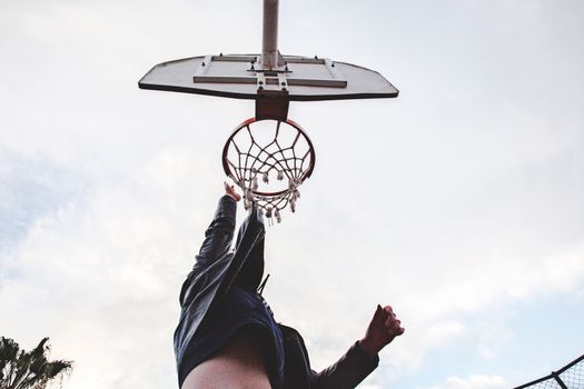 Low angle shot of a person dunking on an outdoor basketball hoop during the day.