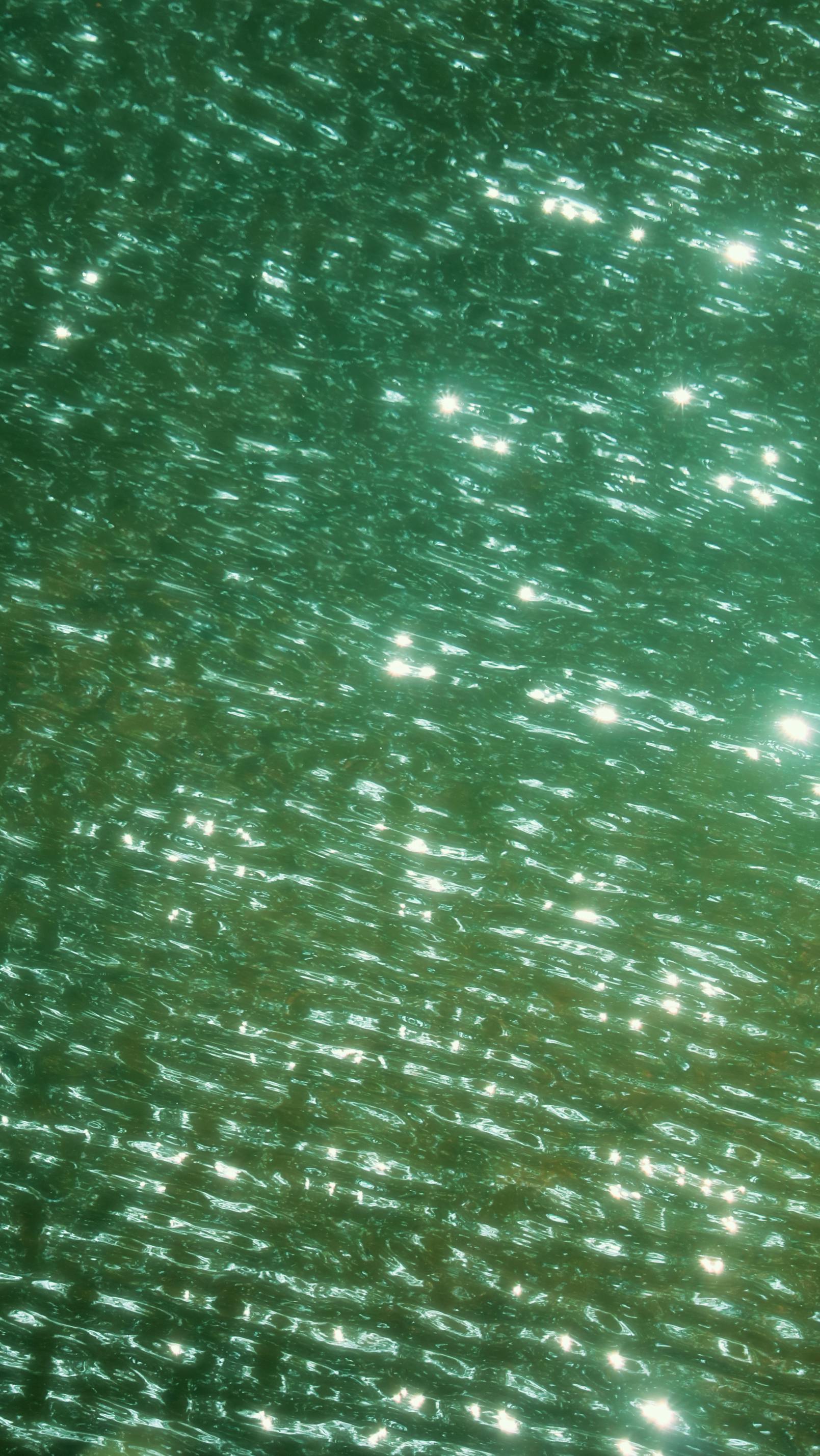 Abstract view of shimmering green water with sunlight reflections creating a peaceful natural texture.