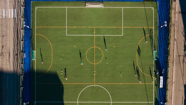 Aerial view of a soccer match on a green field in Alba, showcasing players and shadows.