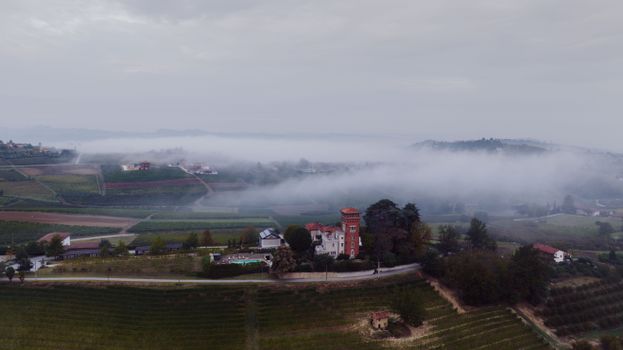 Drone shot of foggy vineyards in Costigliole d'Asti, Piedmont, showcasing beautiful Italian countryside.
