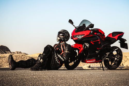 Free A motorcyclist in gear relaxing next to a Kawasaki Ninja on a sunny day. Stock Photo
