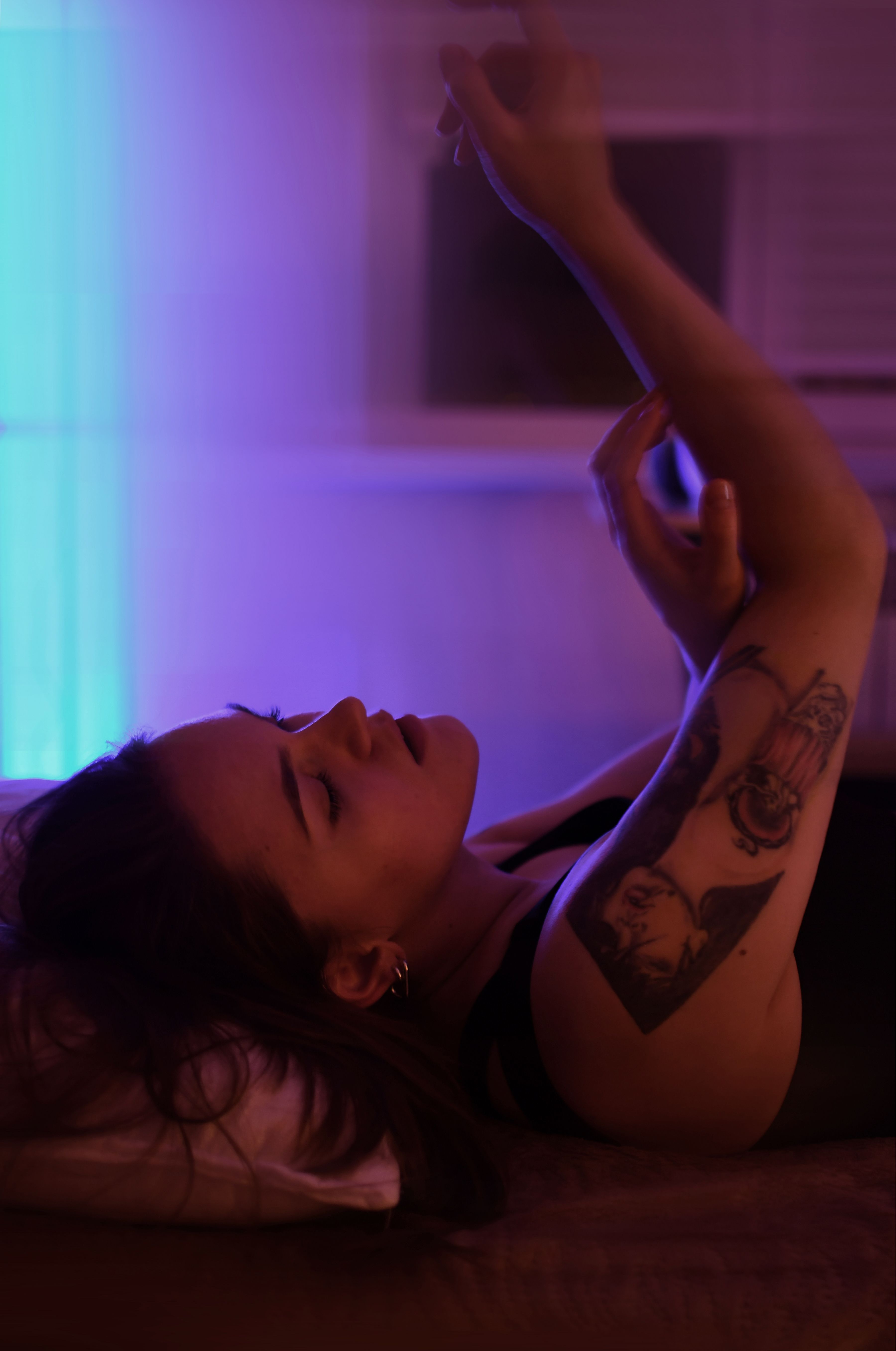 A woman with tattoos lies down, enveloped in mystical purple lighting.
