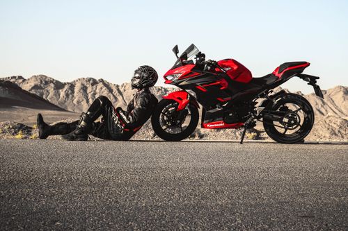 Free Motorcyclist in black gear resting next to a red Kawasaki motorcycle on a scenic mountain road. Stock Photo