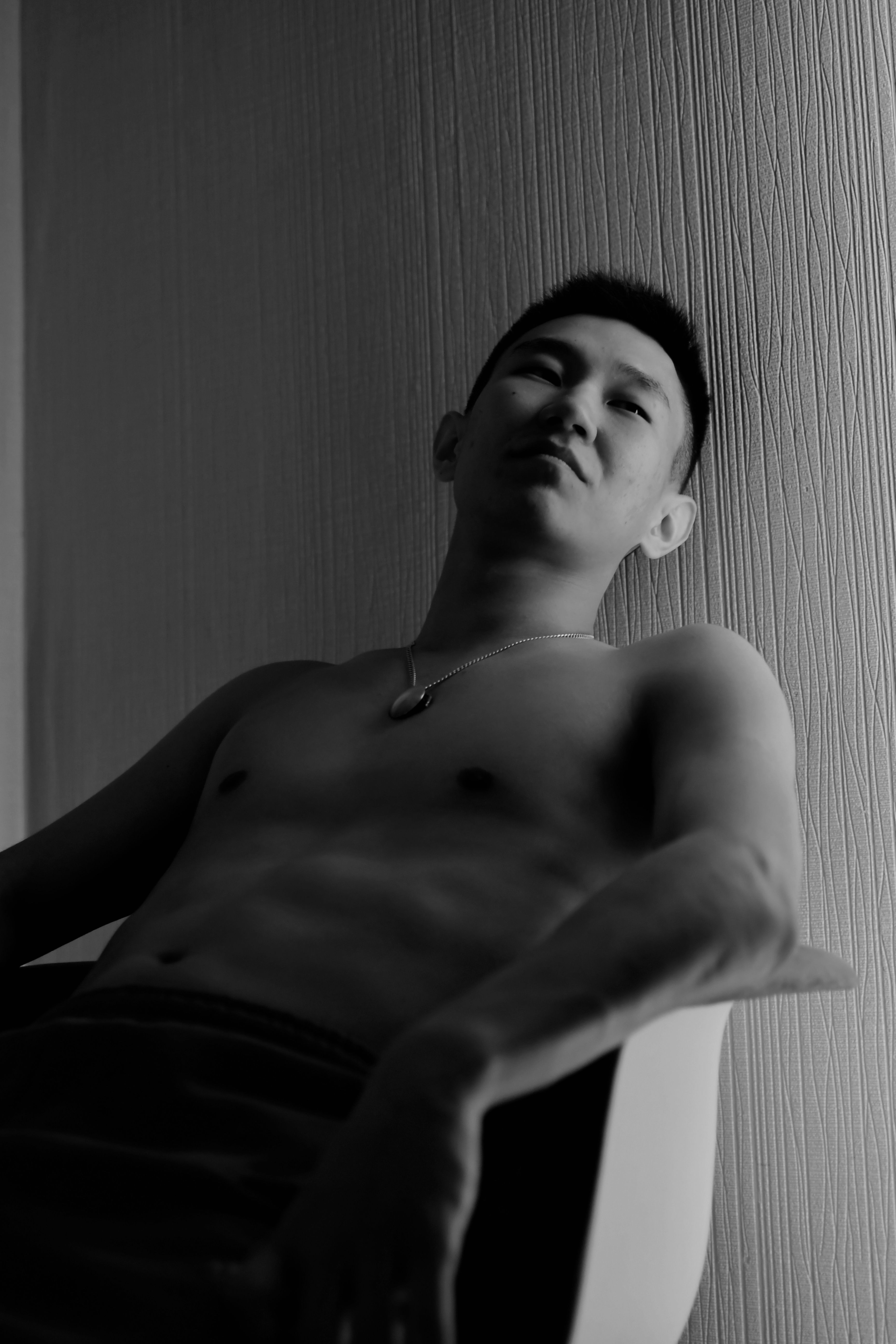 Artistic black and white portrait of a shirtless man sitting in a chair, exuding a calm and contemplative mood.