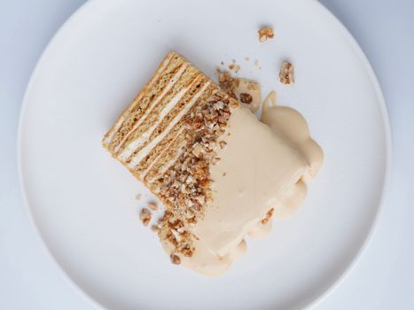 Delicious medovik cake slice with cream and nuts presented on a white plate in top view.