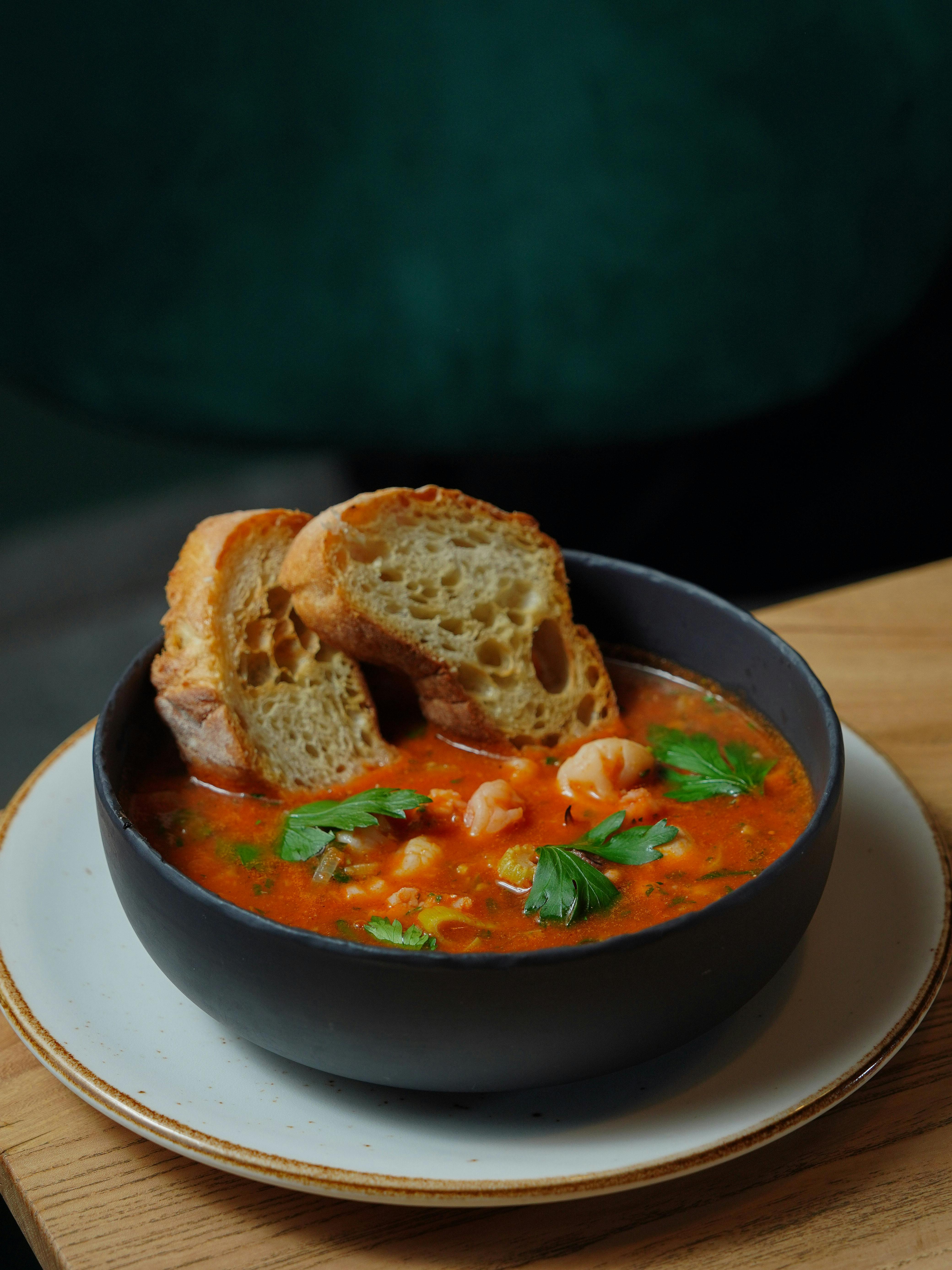 A bowl of delicious-looking soup with fresh herbs and a crusty bread roll.