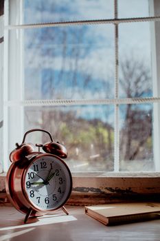 Vintage alarm clock by a sunny window with a notebook, evoking a calm and reflective mood.