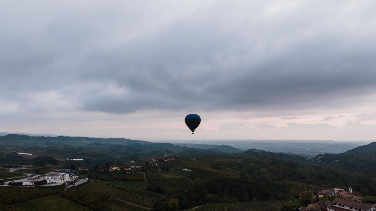 A hot-air balloon drifting over vineyards and villages at dawn