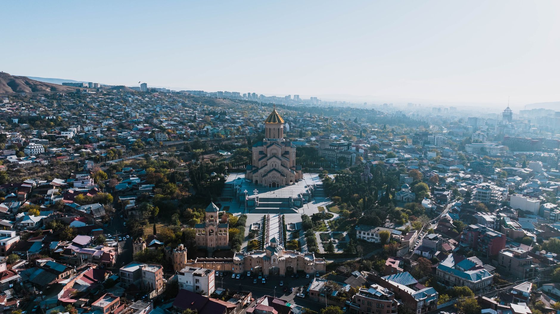 A stunning aerial view capturing the Holy Trinity Cathedral amidst the cityscape of Tbilisi, Georgia.. Photo by K on Pexels