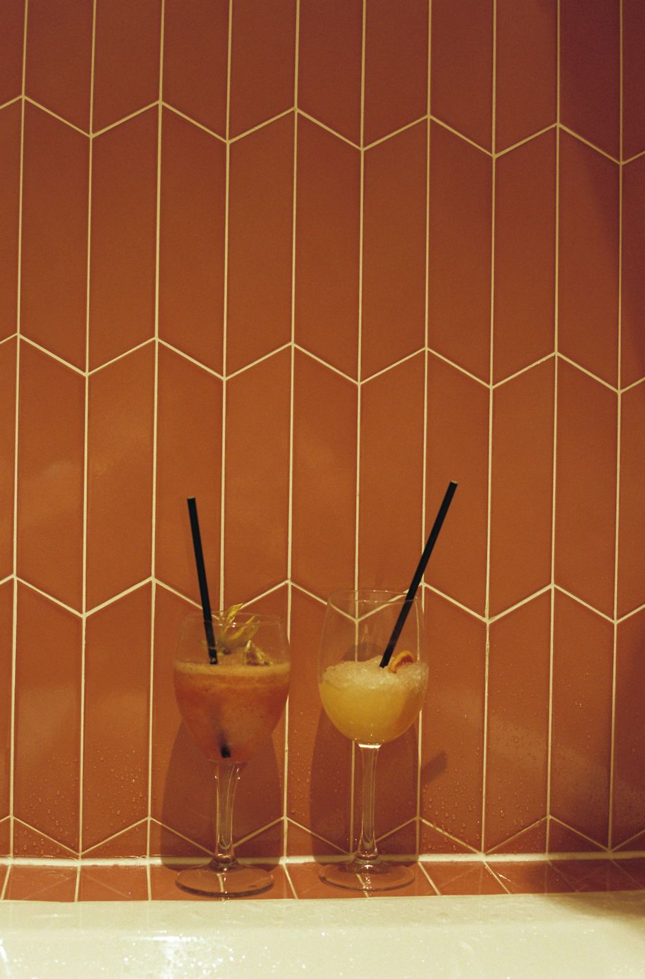 Two colorful cocktails with straws against a stylish tiled wall.