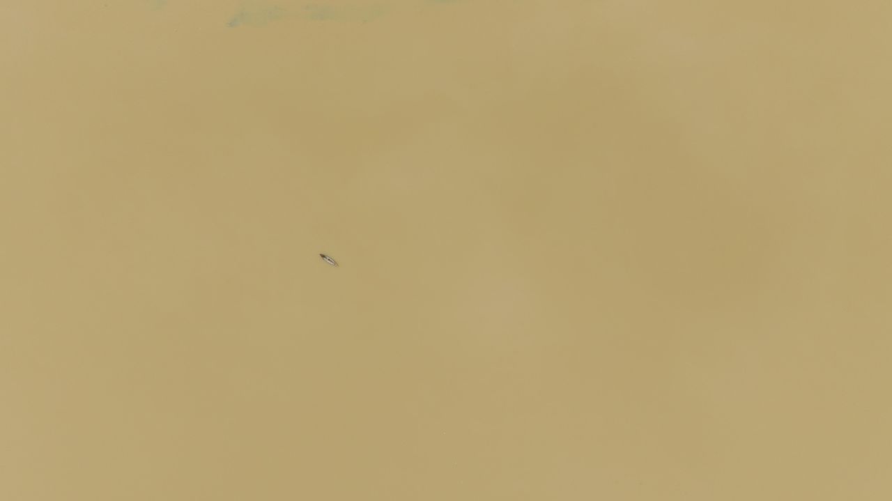 a solitary boat floats on a vast yellow river creating a minimalist ab