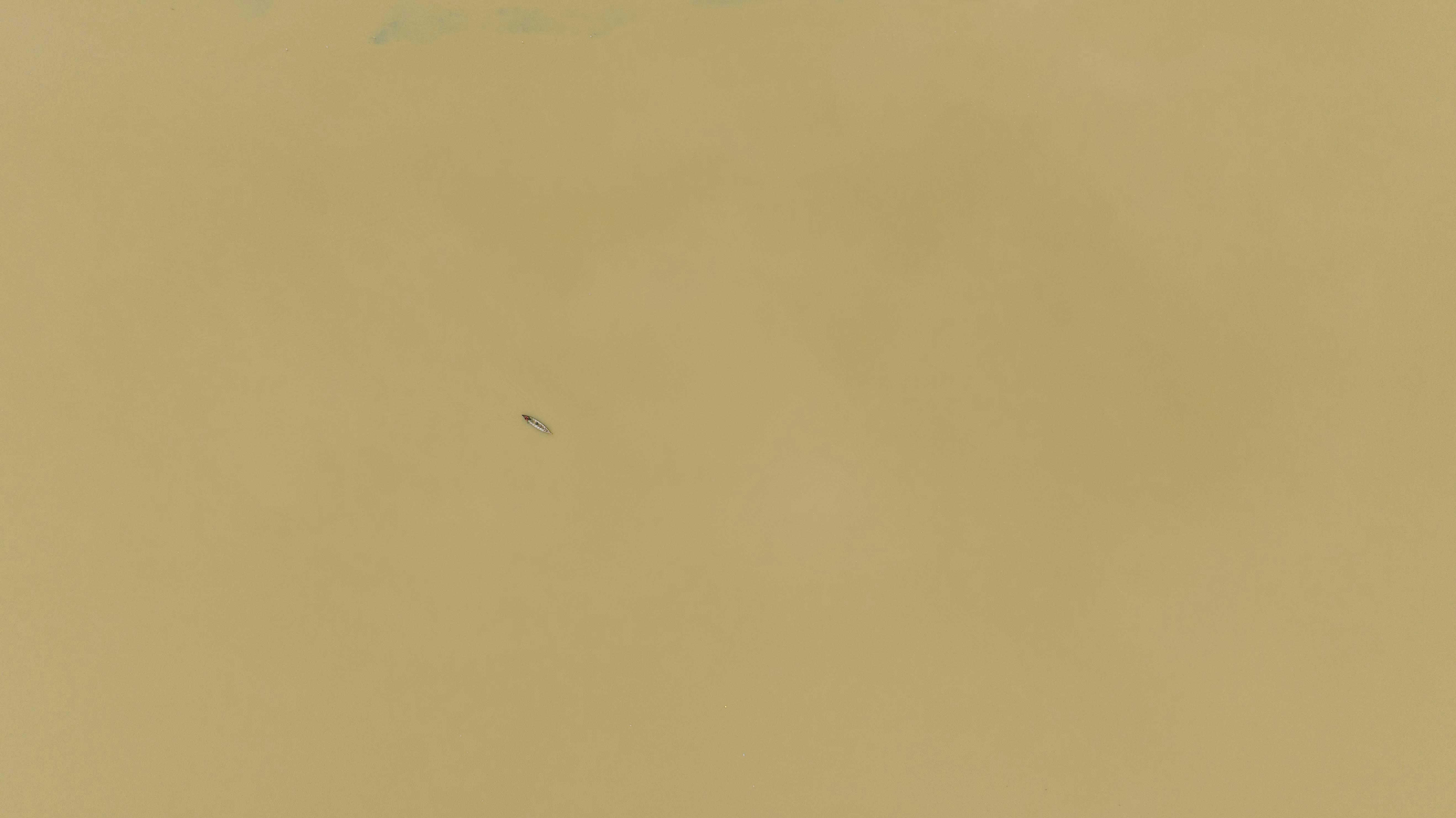 Free A solitary boat floats on a vast yellow river, creating a minimalist abstract scene. Stock Photo