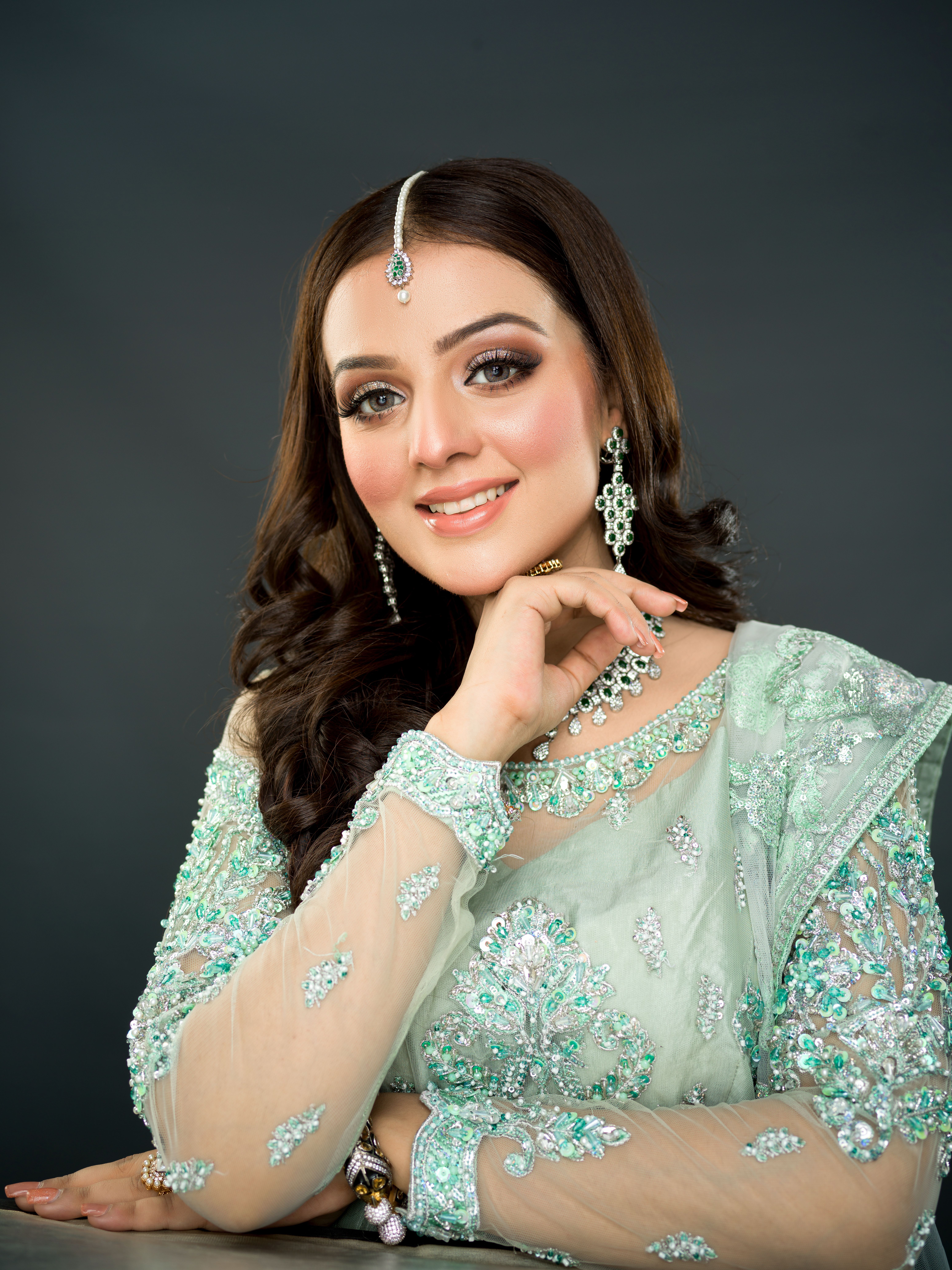 Portrait of a smiling woman in green traditional dress with jewelry against a gray background.