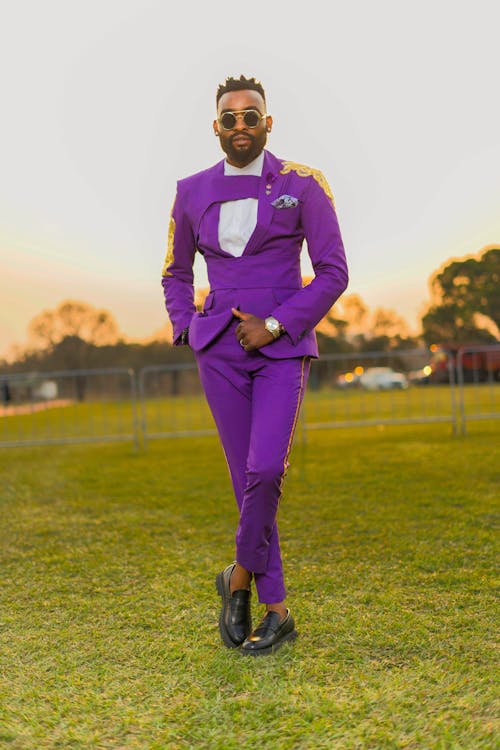A Man in a Purple Suit Standing on a Meadow at Sunset