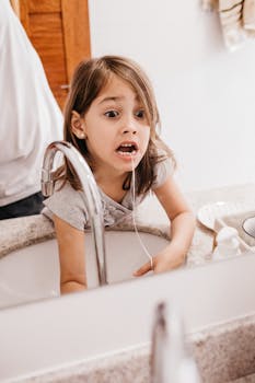A young girl learns dental hygiene by flossing her teeth in the bathroom mirror.