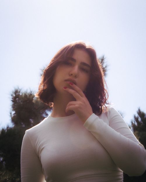 Free Young woman in white sweatshirt posing thoughtfully outdoors on a sunny day. Stock Photo