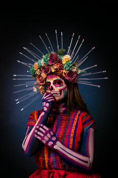 Colorful Day of the Dead makeup with a floral headdress in a studio setting.