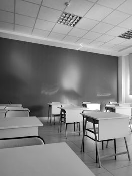 A minimalist black and white image of an empty classroom with desks and chairs.