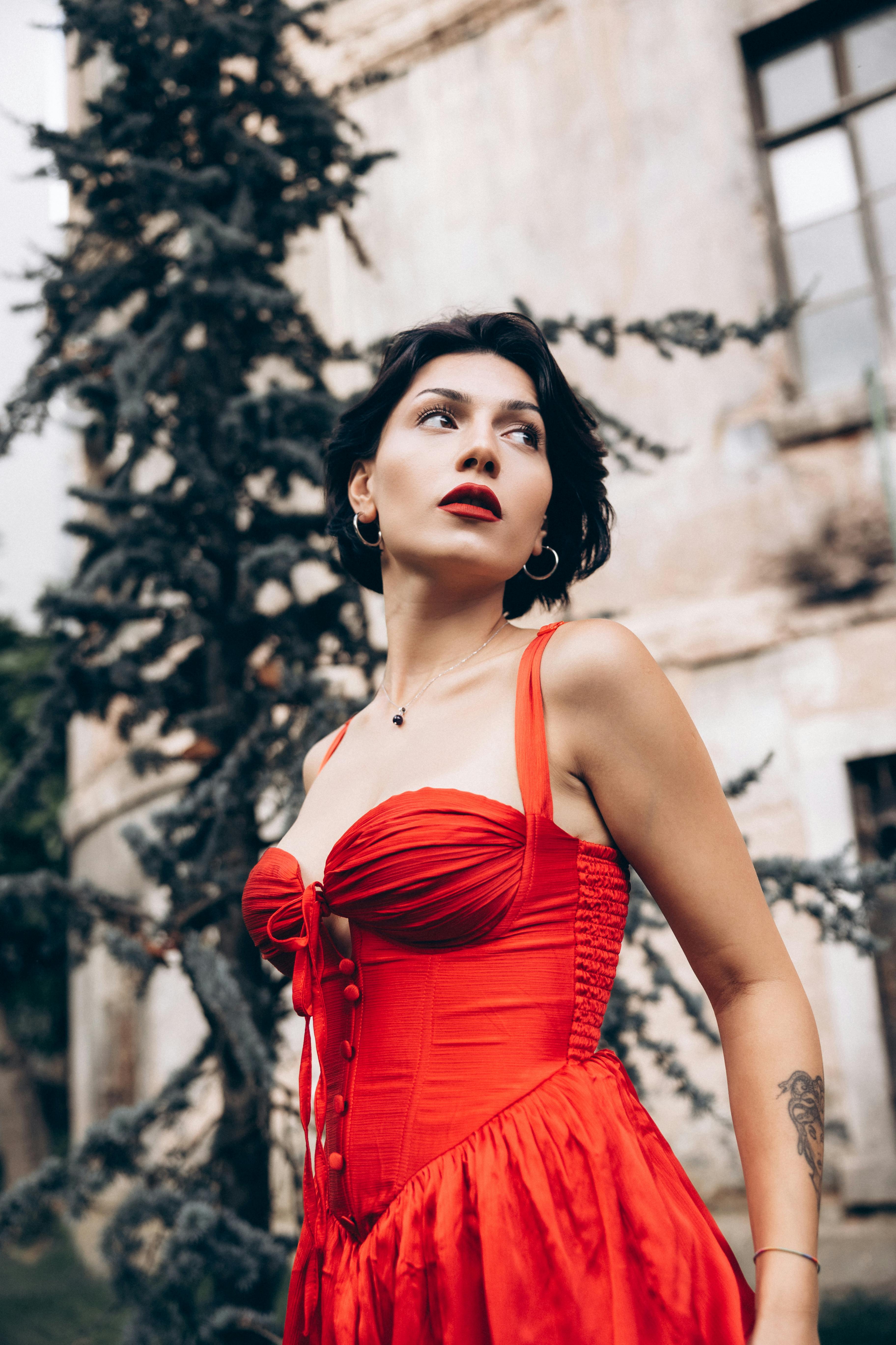 a woman in a red dress standing in front of a tree