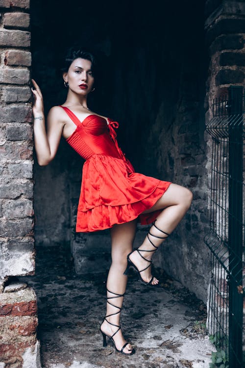 A woman in a red dress posing in front of an old brick wall