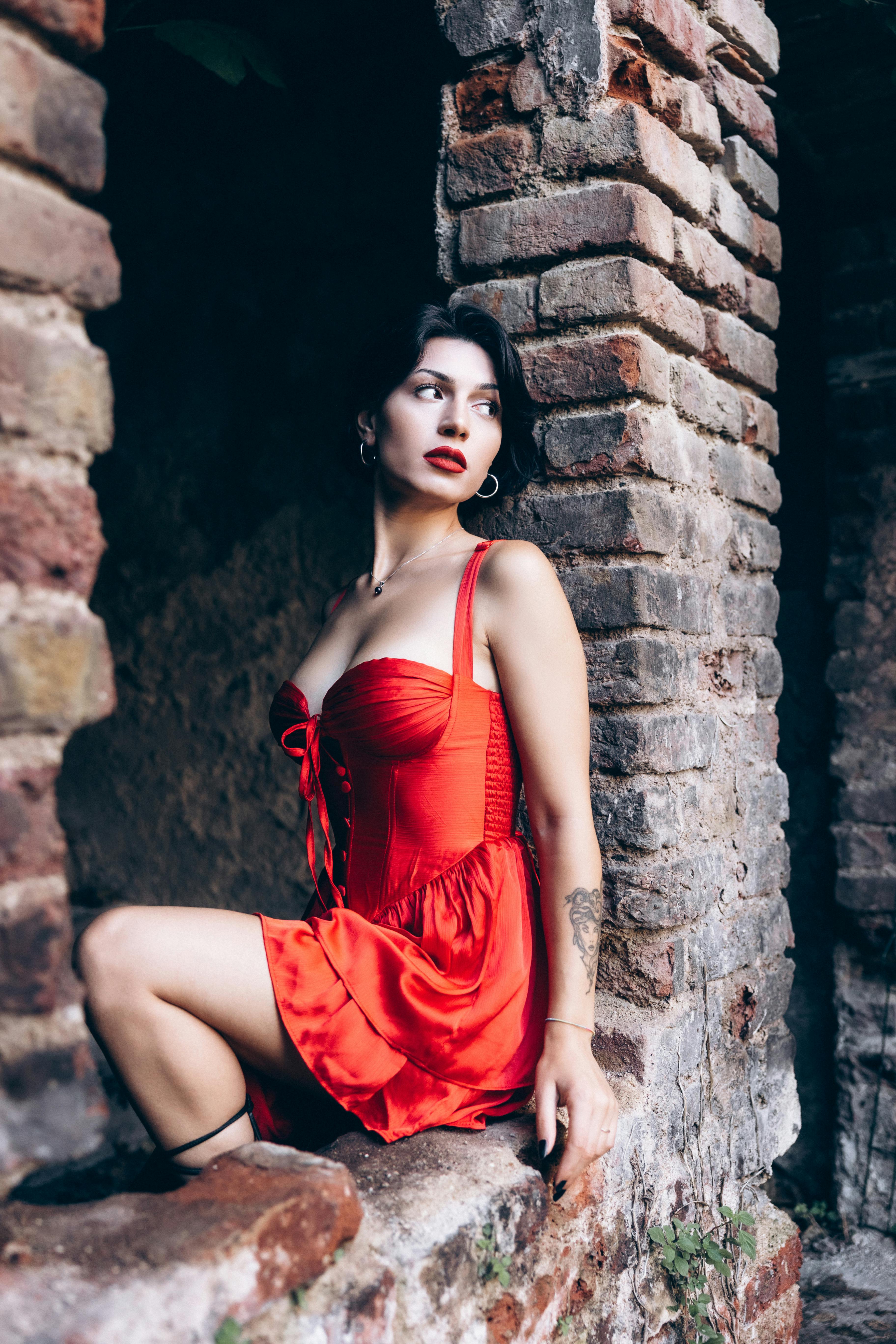 a woman in a red dress sitting on a brick wall