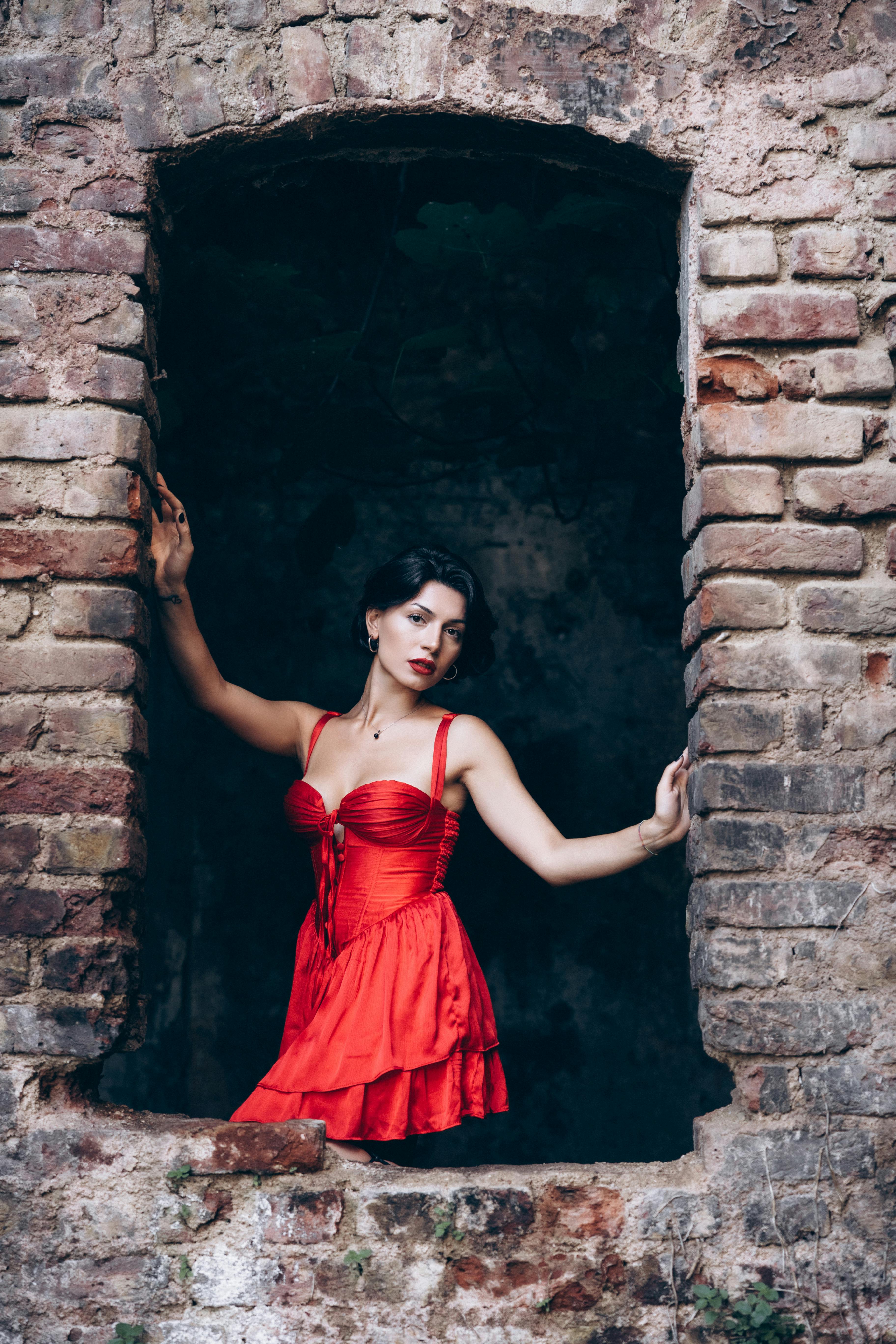 a woman in a red dress is standing in an old brick wall