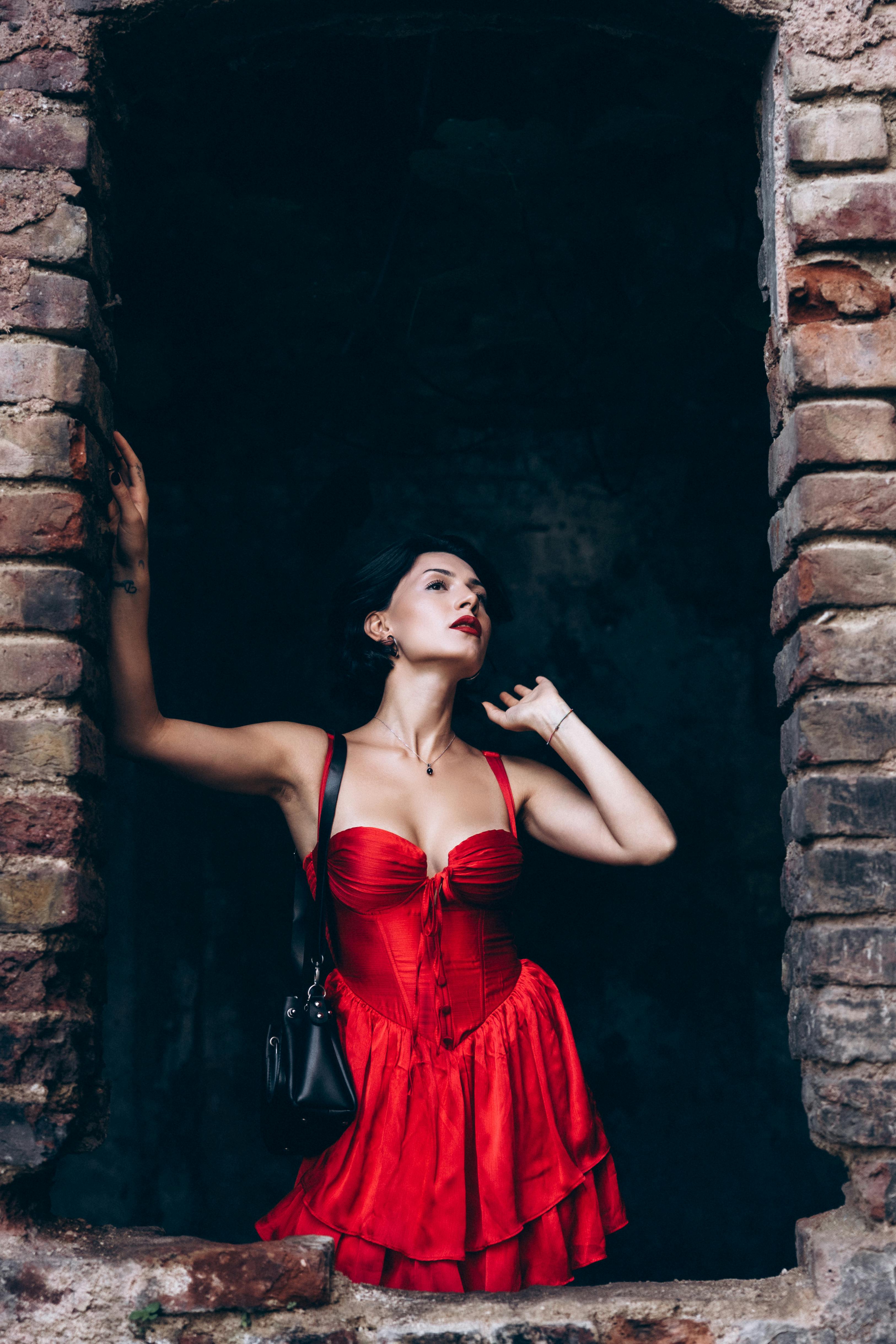 a woman in a red dress is standing in an old brick wall