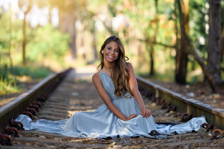 Smiling Model In Blue Dress Sitting On Railway Tracks