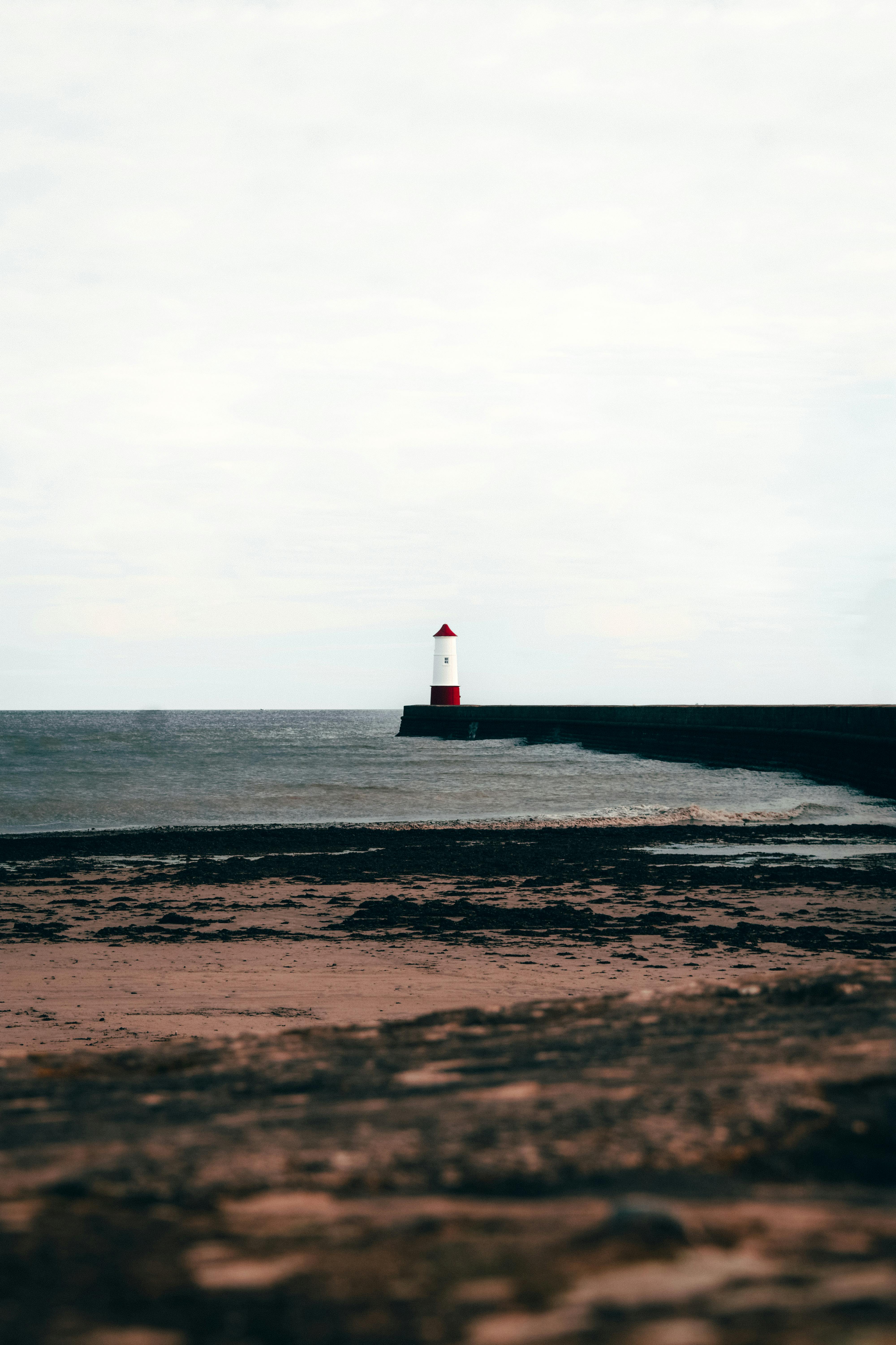 Iconic Berwick Lighthouse standing tall by the sandy shore on a cloudy day.