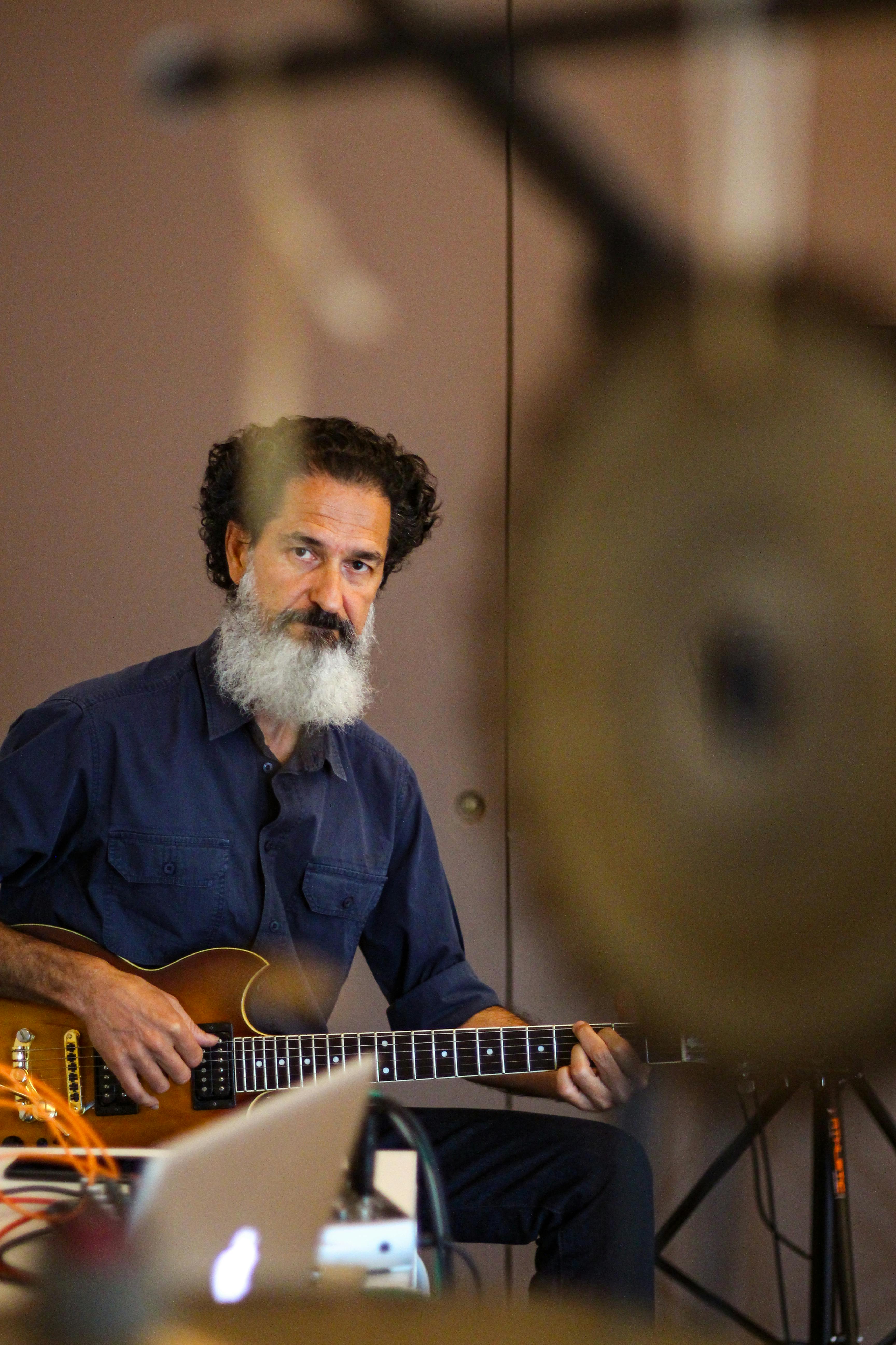 Elderly man with a beard playing an electric guitar indoors, capturing a musical moment.