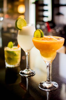 Three vibrant citrus cocktails with lime garnishes on a glossy bar counter, perfect for a summer vibe.